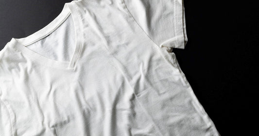A white t-shirt resting on a black surface, accompanying instructions for shrinking cotton t-shirts at home.