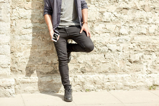 A man leans against a wall in skinny jeans, contemplating whether this trend is still in style for men.