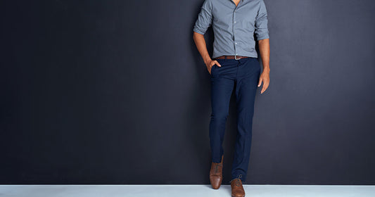 A man wearing a blue shirt and navy blue pants stands, showcasing a stylish outfit combination.