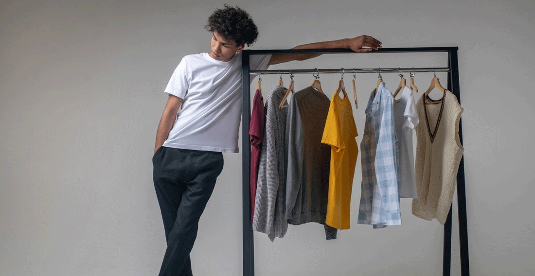 A man casually leans against a clothing rack, surrounded by various men's outfits