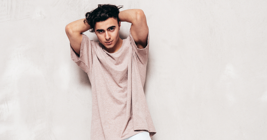 Man in an oversized T-shirt posing against a plain wall. 